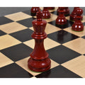 Close-up of a burgundy lacquered boxwood Prime Staunton king on a chessboard, with other red pieces blurred behind it.