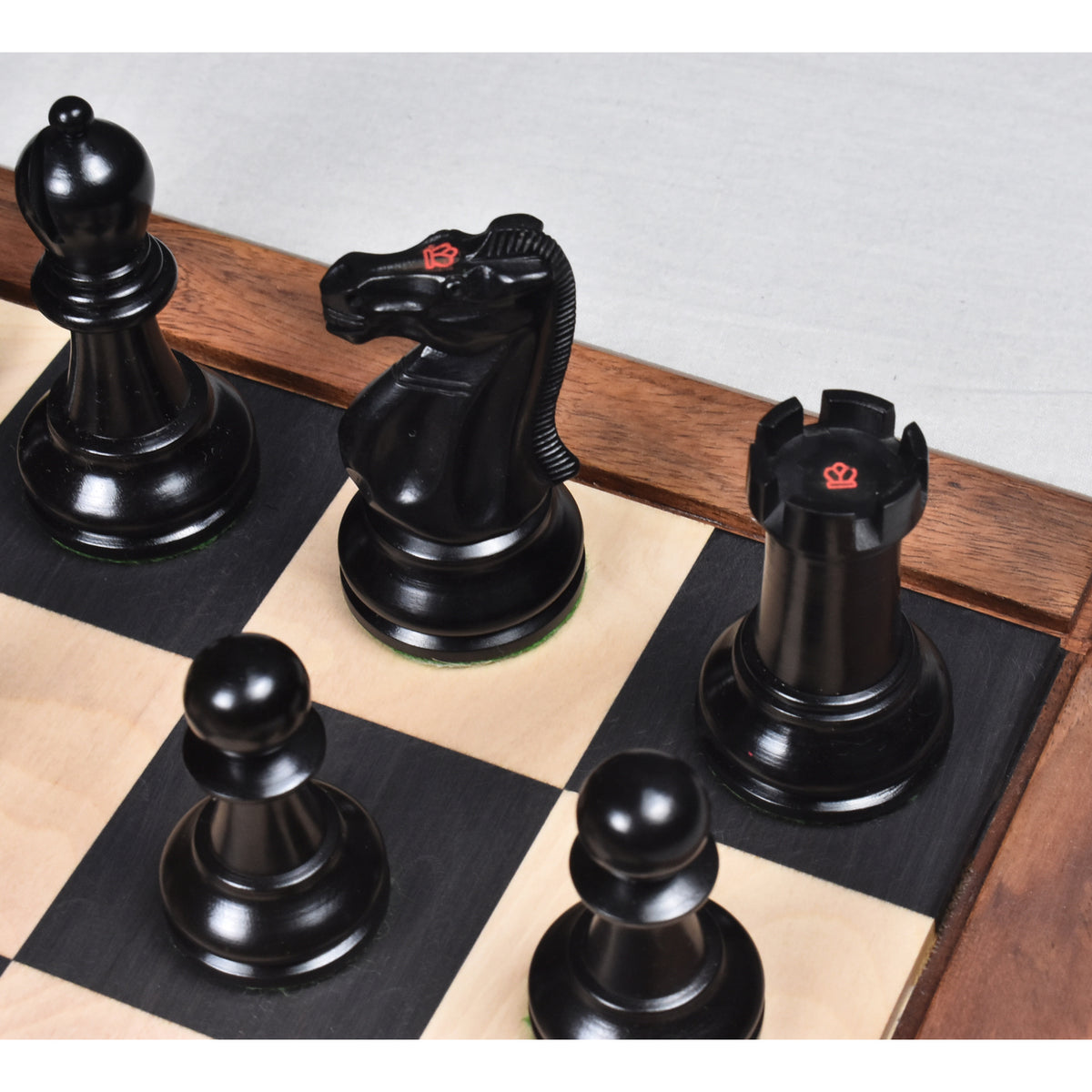 Black ebony knight with a red crown stamp next to a rook and bishop on a wooden chessboard.