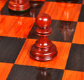 Close-up of an elegant Bud Rosewood Staunton pawn piece resting on a high-quality wooden board.