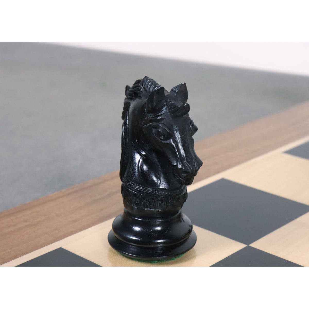 A striking front-facing view of a detailed ebony Staunton knight placed on a wooden chessboard.