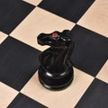 Overhead view of a black ebony knight piece with a distinct red crown marking on a chess board square.