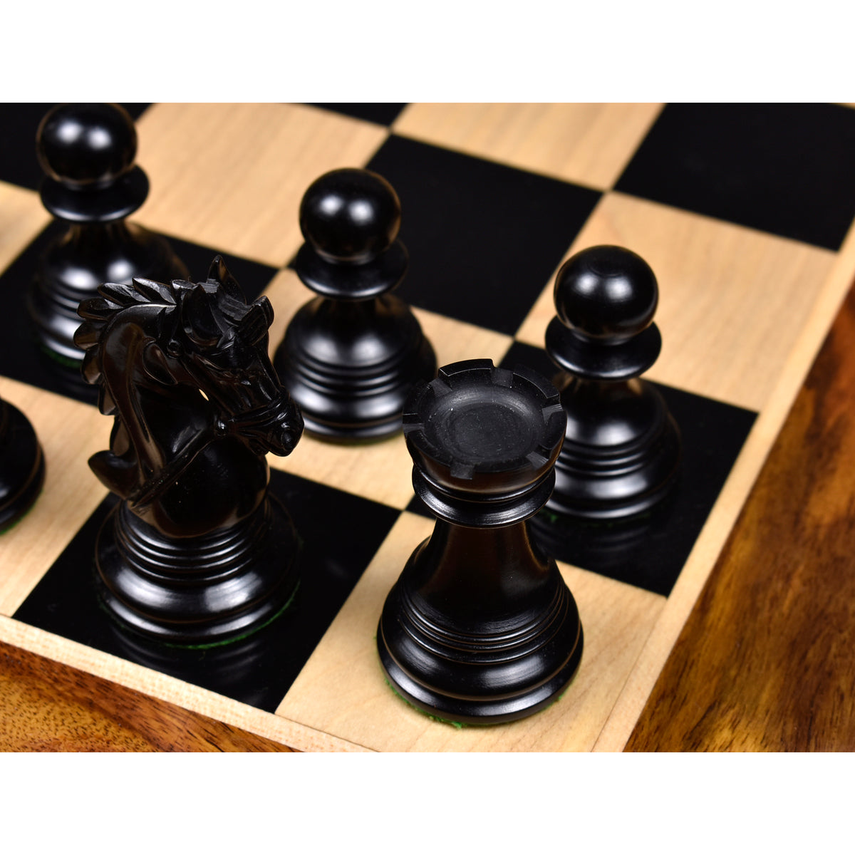 Detailed top view of an ebony wood knight, rook, and pawns on a glossy luxury wooden chessboard.