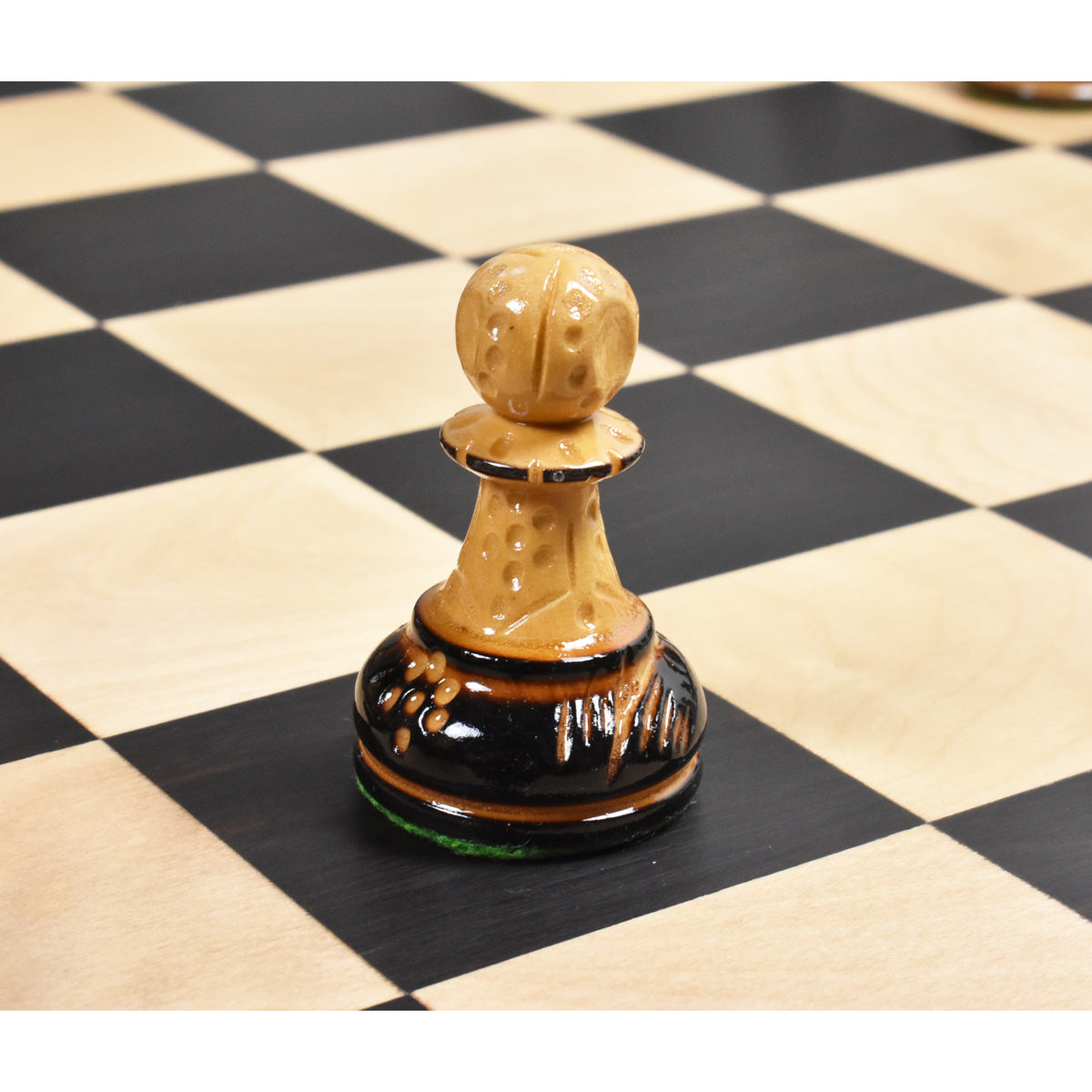 Macro shot of a Dubrovnik pawn chess piece in natural boxwood with a burnt ebonized base on a wooden chessboard.