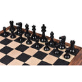 Full army of black ebony Lessing Staunton chess pieces lined up on a modern wood chessboard.