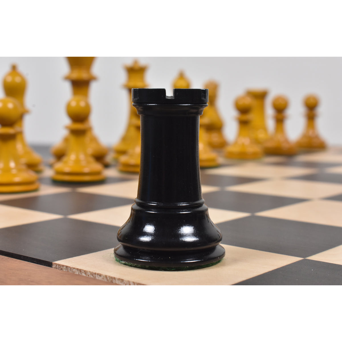 Black ebony Harrwitz Staunton rook chess piece standing on a wooden board.