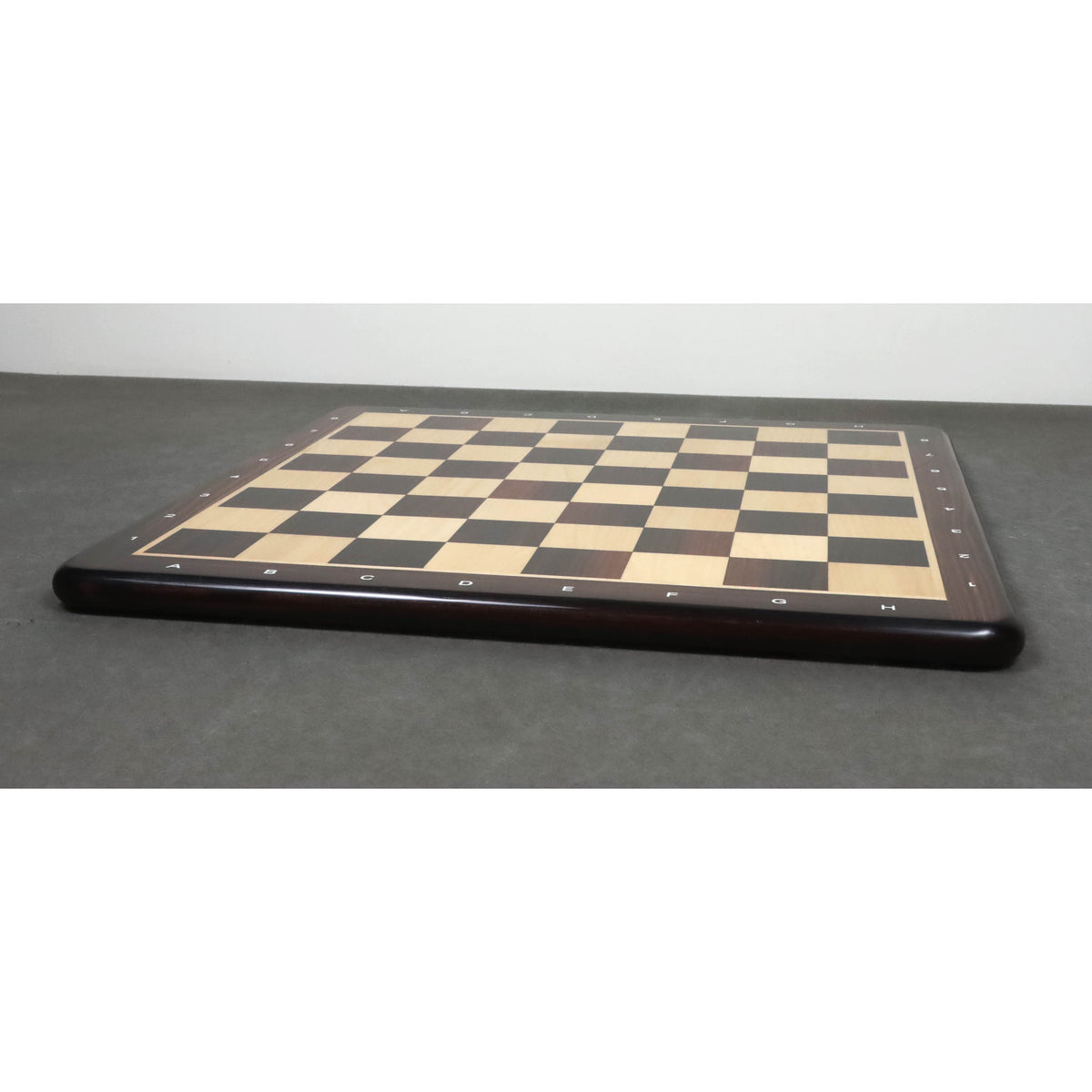 Perspective view of a 19 inch flat rosewood and maple wood chessboard on a grey surface.