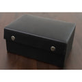Closed black leatherette chess piece storage box with button fasteners on a wood surface.