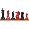 Red and black Staunton chess pieces lined up on a wooden surface.