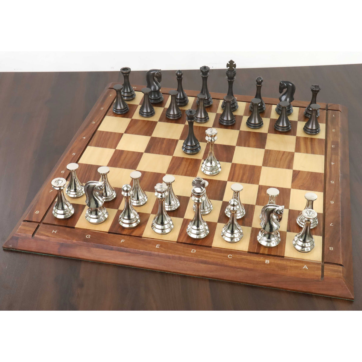 Silver and antique finish luxury metal chess pieces arranged on a premium wooden chess board.