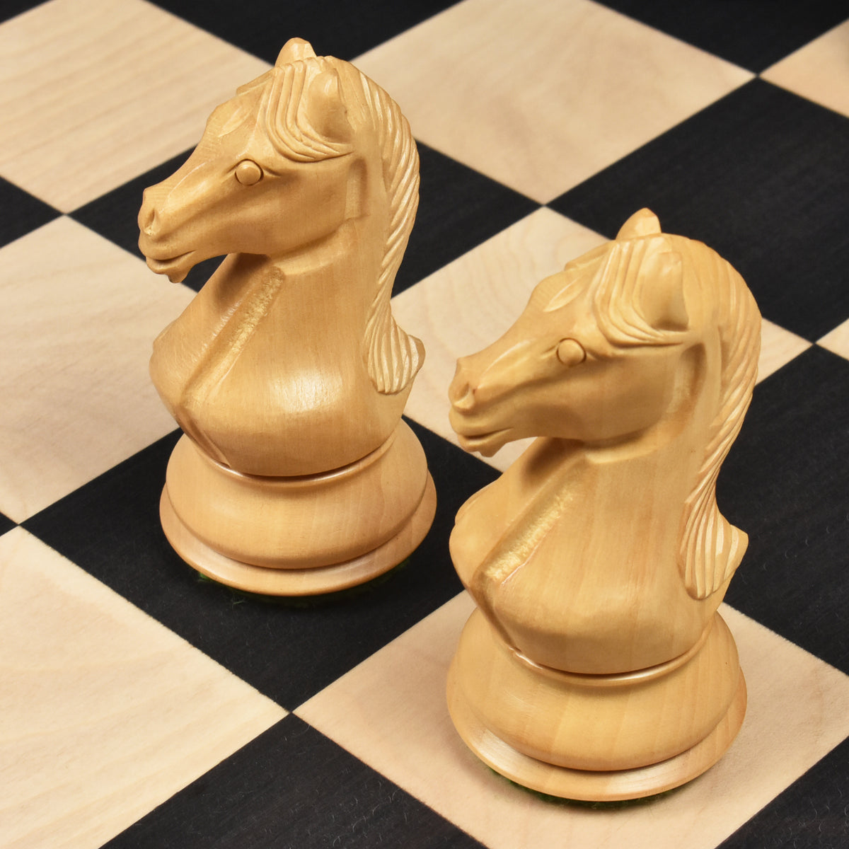Pair of finely detailed boxwood Staunton knight chess pieces on a wooden chess board.