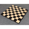 An empty black and maple wooden chessboard viewed from a high angle.