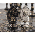 Close-up face-off between one intricately carved silver brass Knight and one black brass Knight on the decorative metal board.