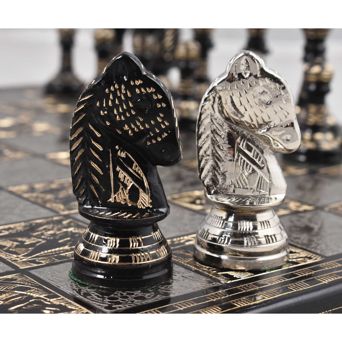 Close-up face-off between one intricately carved silver brass Knight and one black brass Knight on the decorative metal board.