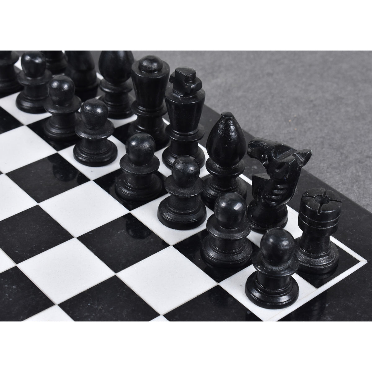 Close-up of black marble chess pieces arranged on a stone chessboard.