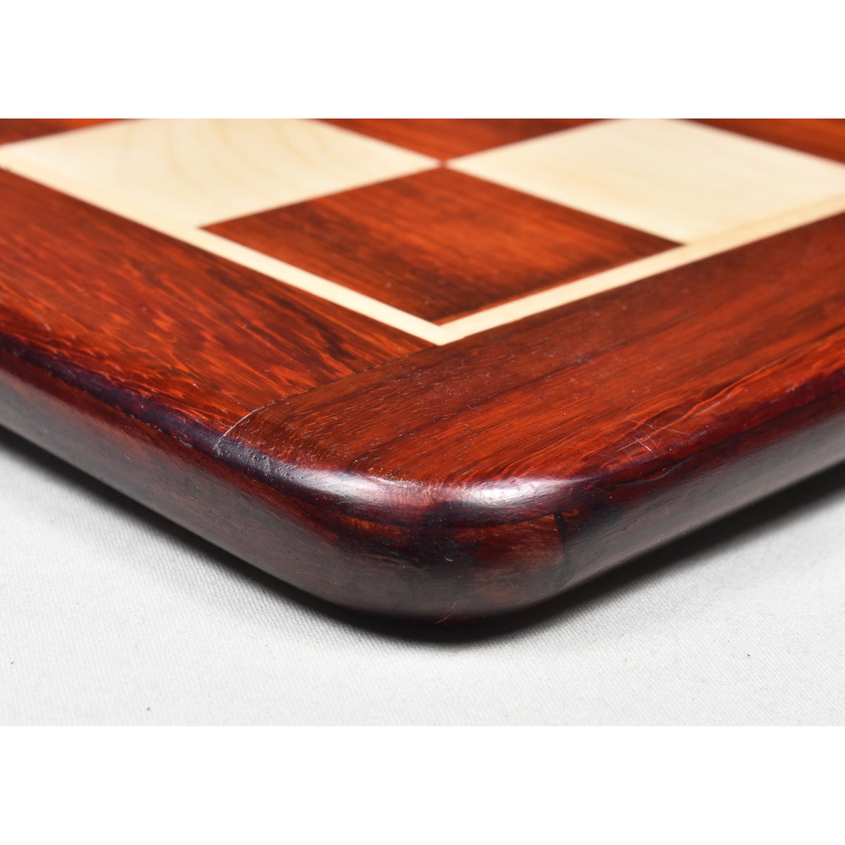 Extreme close-up of the smooth, glossy rounded corner edge of a Bud Rosewood chess board.