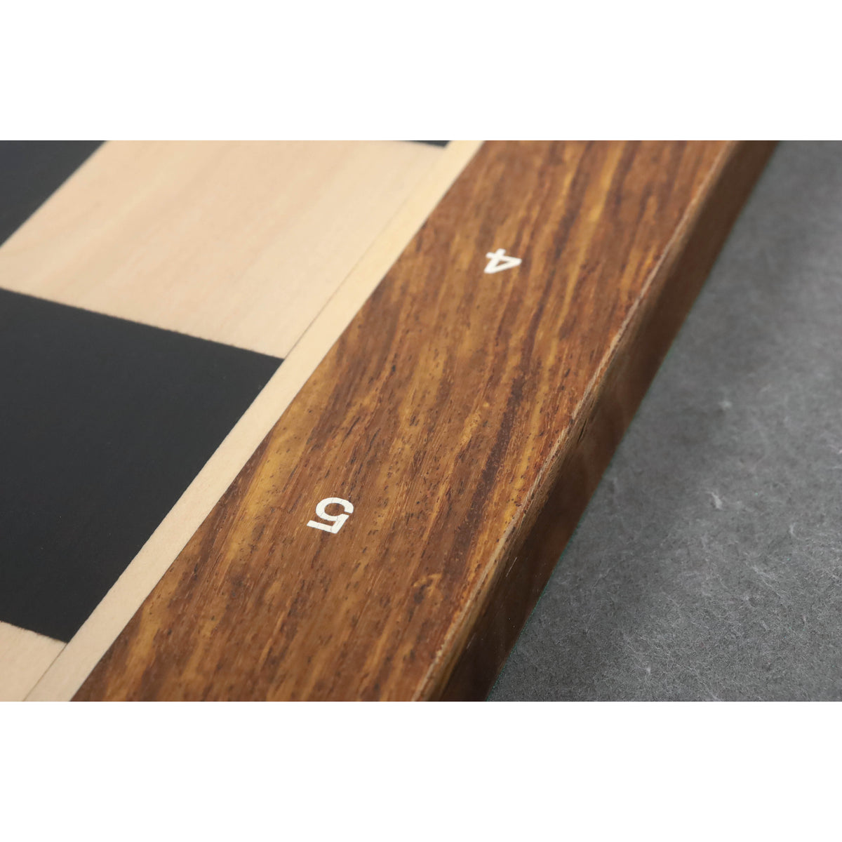 Macro shot of laser-engraved algebraic notations on the border of an Ebony and Maple chessboard.