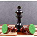 An upright ebony king behind two fallen bud rosewood chessmen, highlighting the thick green felt bases.