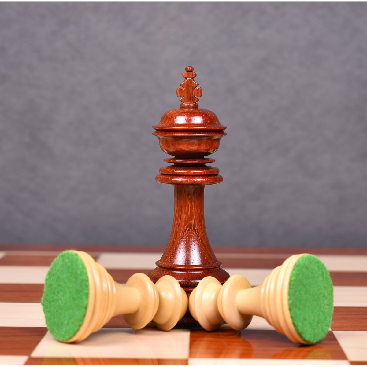 Crimson bud rosewood King piece flanked by two overturned boxwood pieces showing green felt bases.
