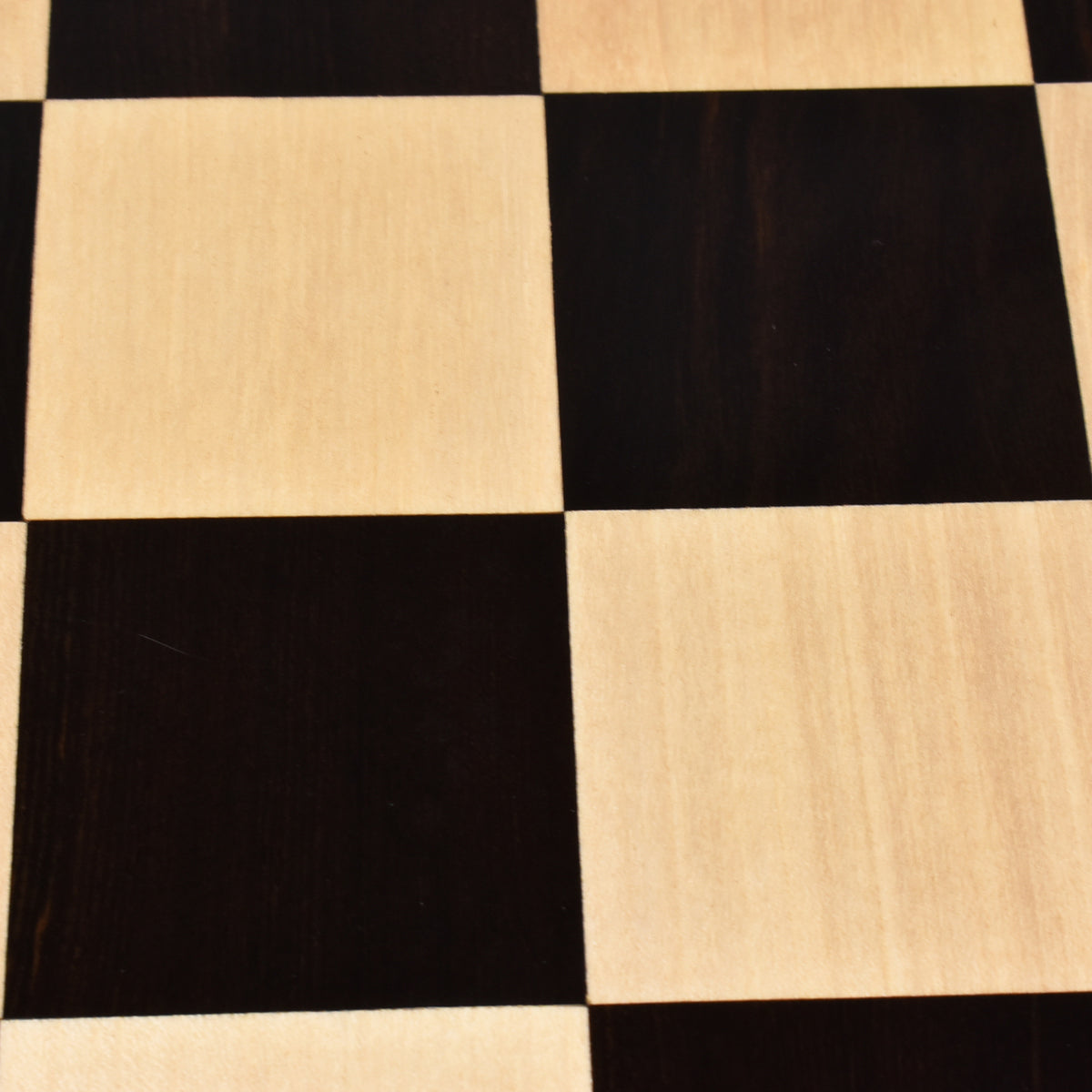Extreme close-up of the alternating dark ebony and light maple squares on the premium solid wooden chessboard.