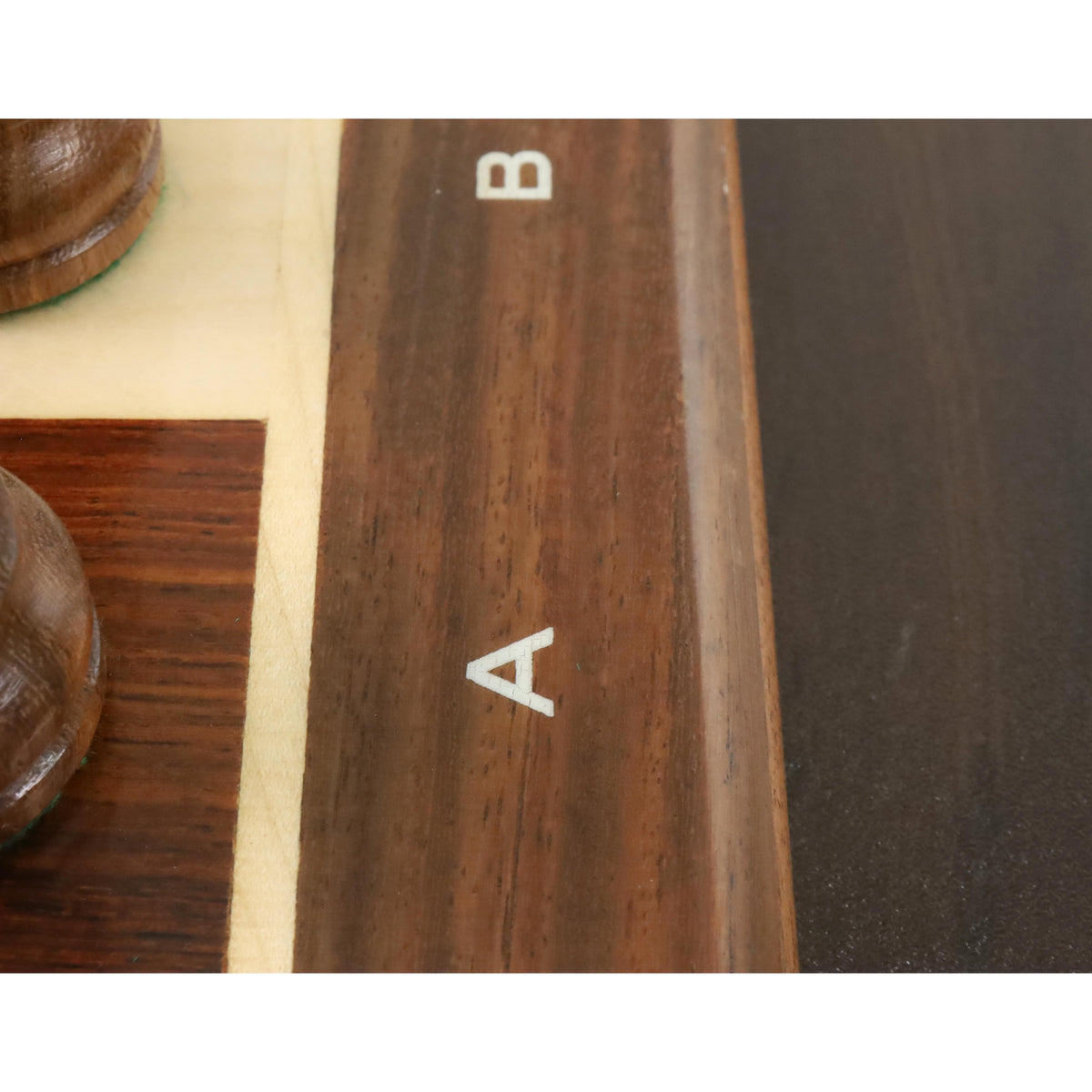 Close-up view of the clean rank and file letter engravings on the wooden border of the chess board.