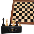 Spartacus ebony chess pieces arranged on a black coffer box with a 23-inch wooden chessboard behind them.