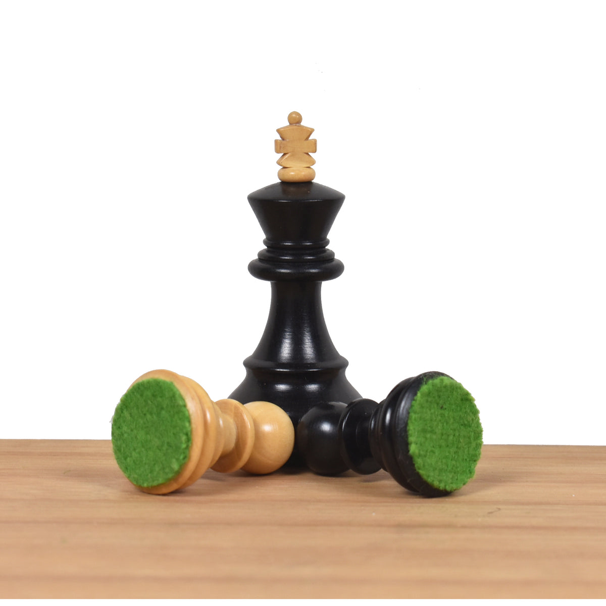 Black ebonised king standing over tipped pieces highlighting the protective green felted bases.