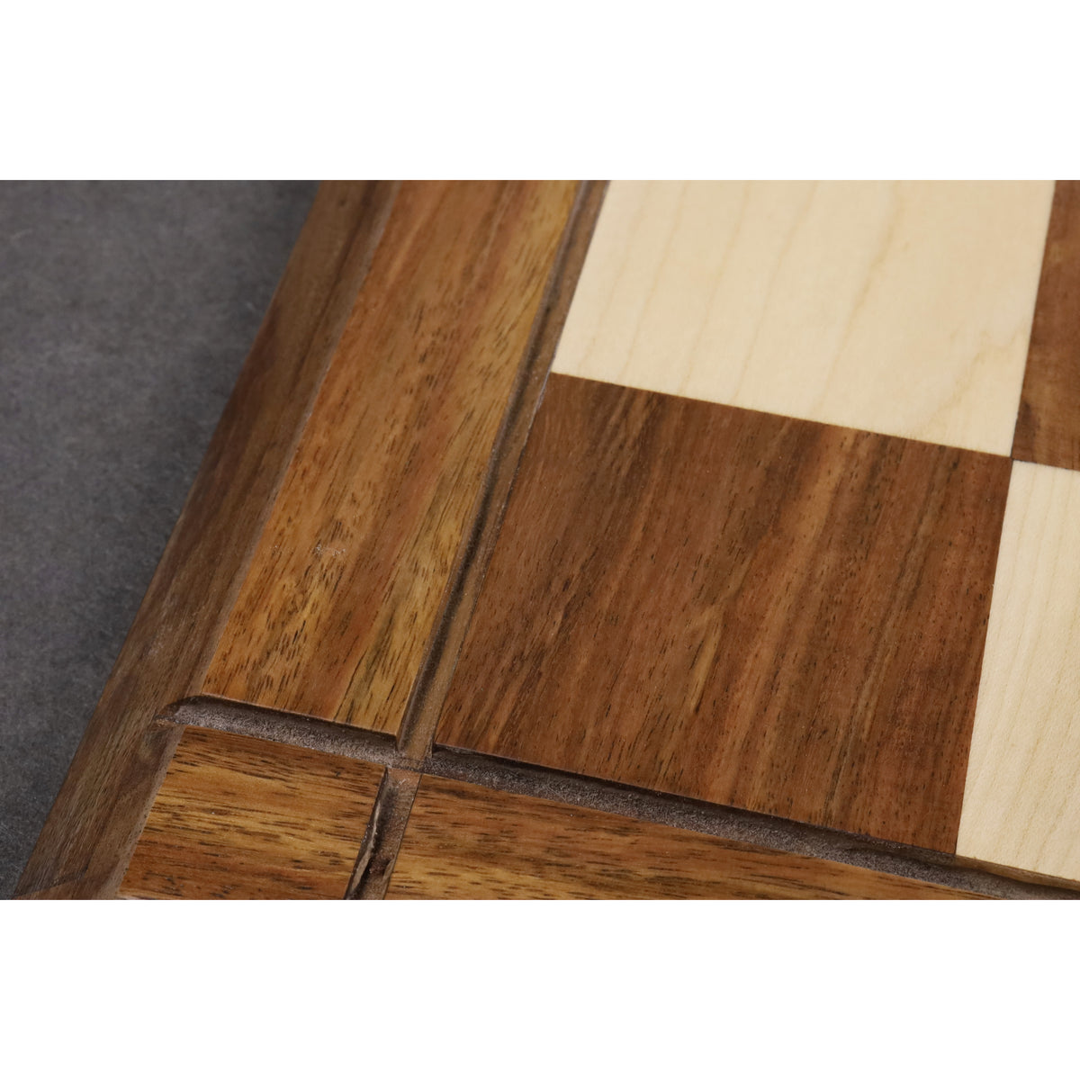 Extreme close-up of the natural wood grain and precision joinery on the Golden Rosewood and Maple chess board.