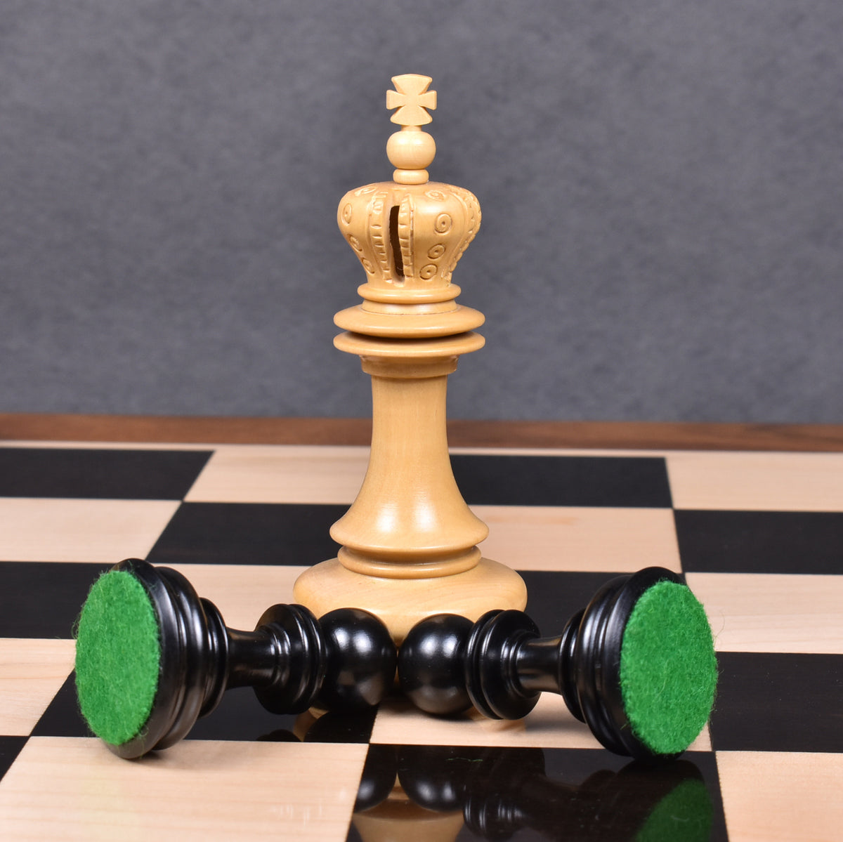 Close-up of a carved boxwood king with black pieces featuring green felt bases.