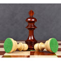 A bud rosewood king piece standing next to two horizontal boxwood pawns revealing green felt bases.