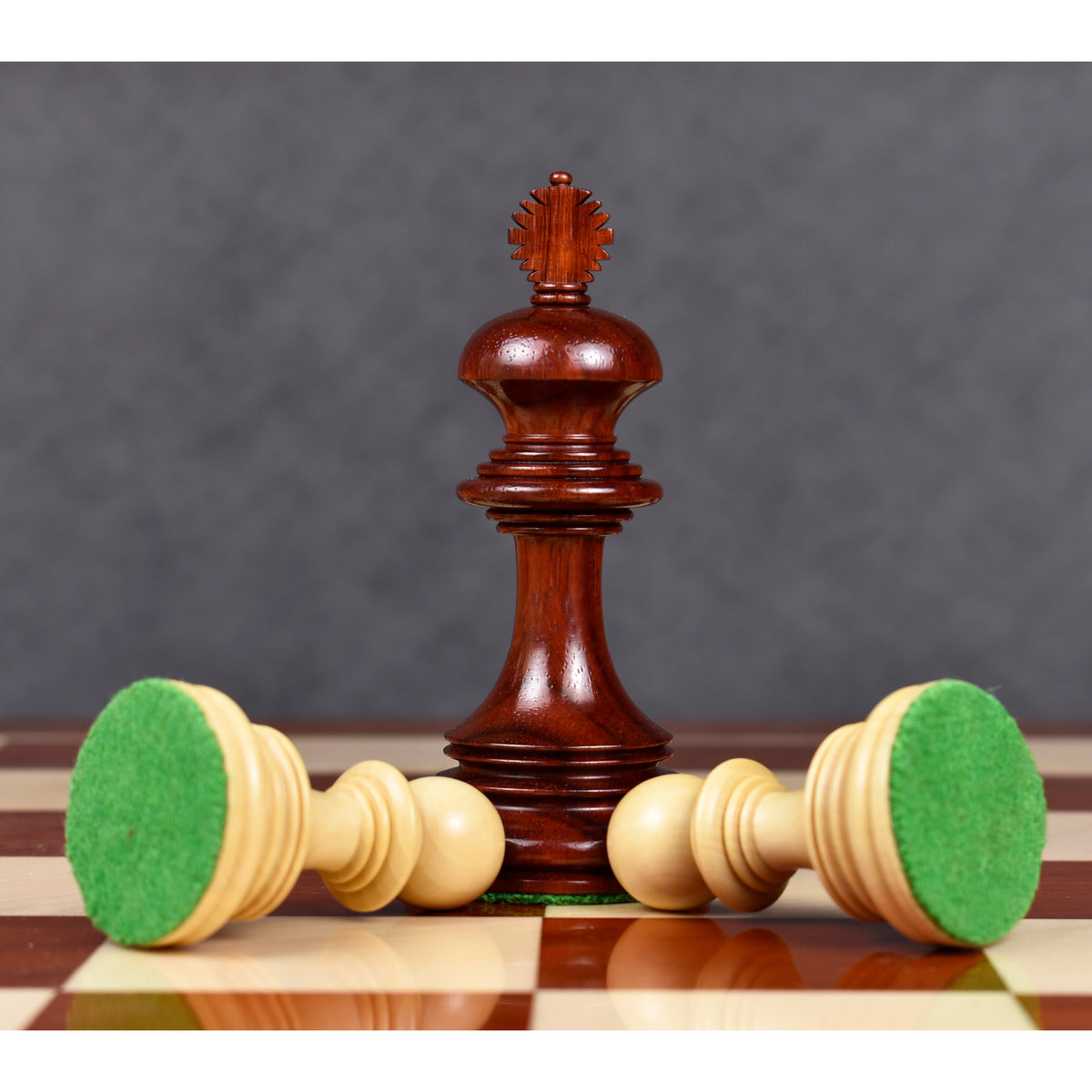A bud rosewood king piece standing next to two horizontal boxwood pawns revealing green felt bases.