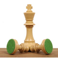 A natural boxwood W.T. Pinney standing King rests upon two horizontally laid pieces, displaying their green felt bases.