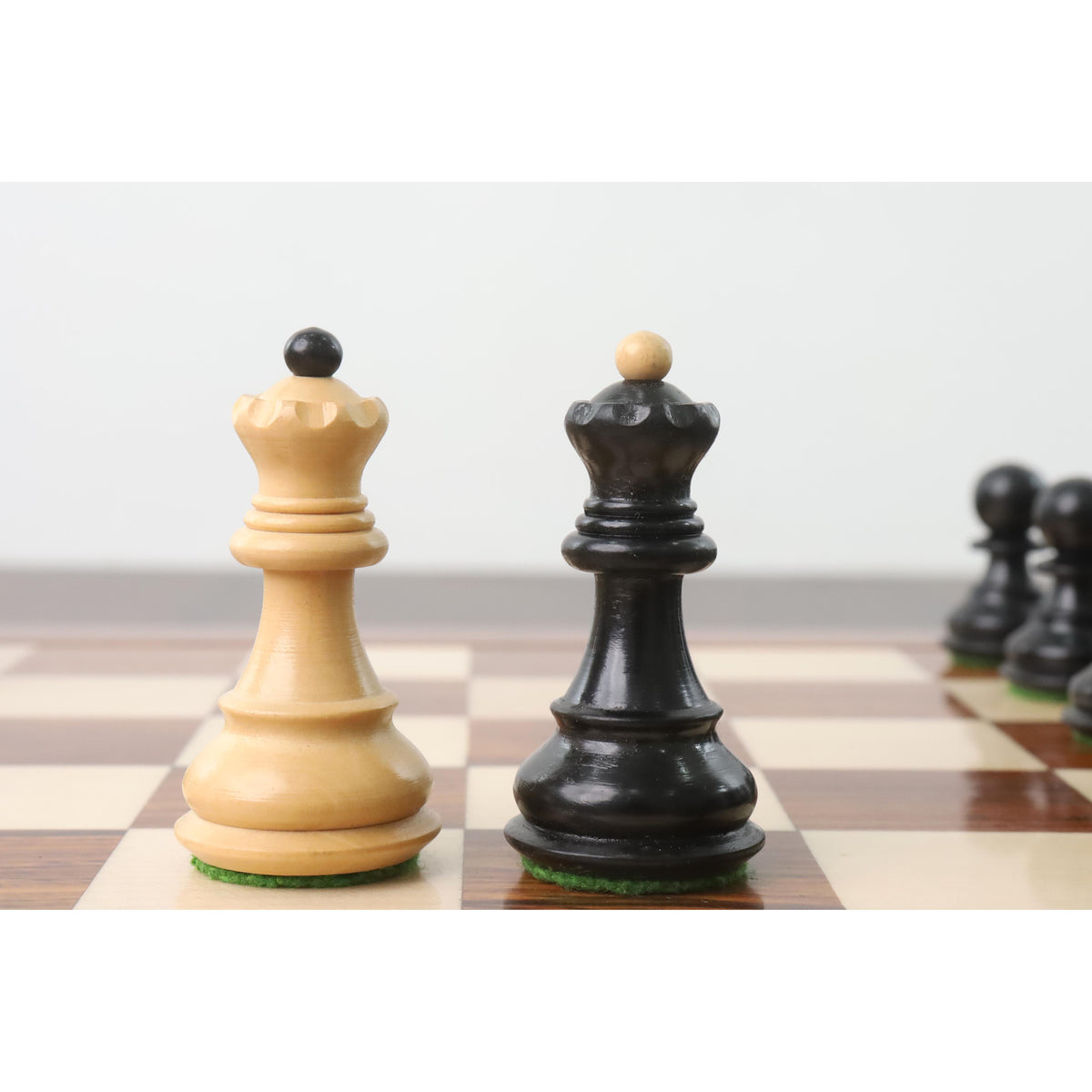 Ebonised and natural boxwood queens from the Zagreb collection displayed on a premium chess board.