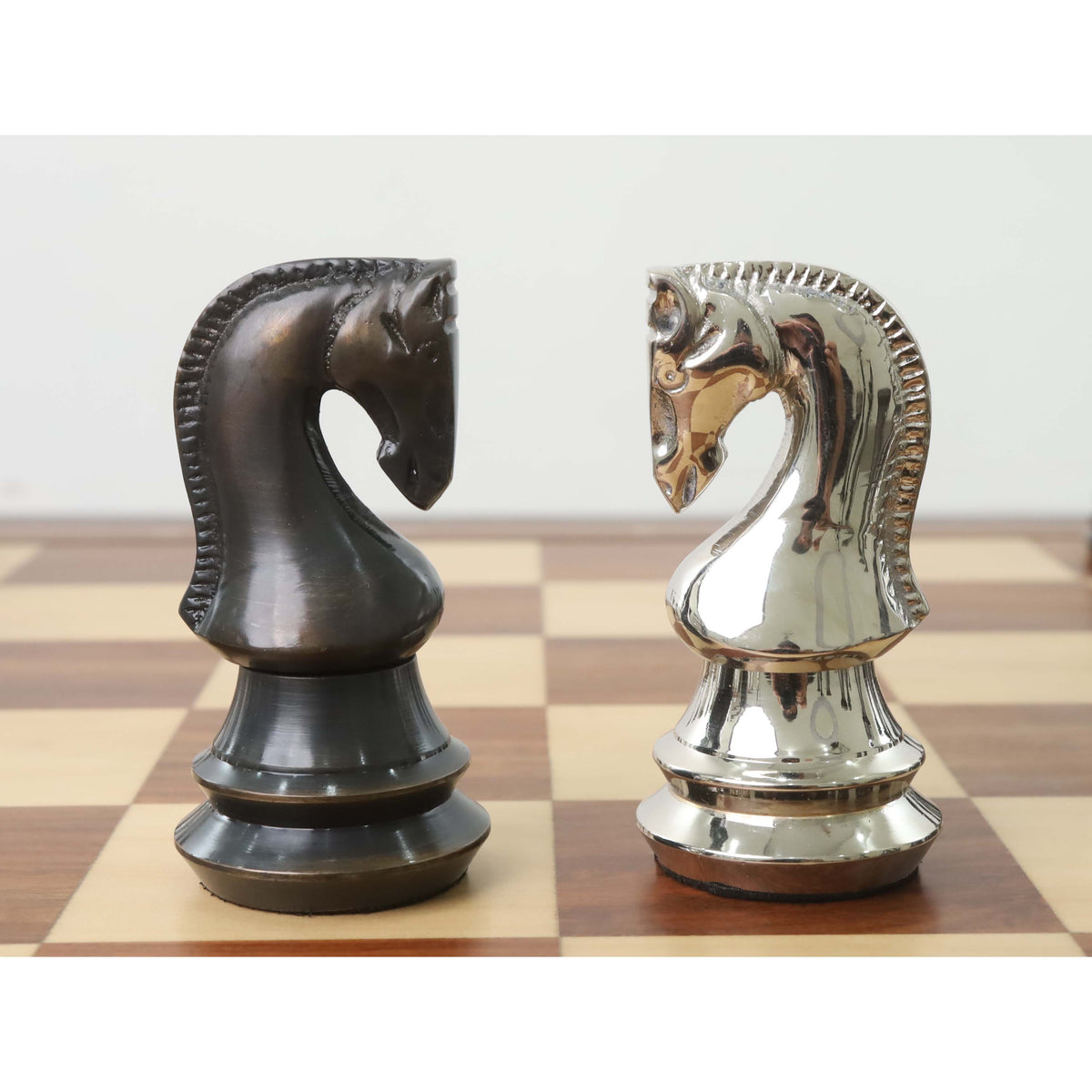 Profile view of antique and silver brass metal luxury chess knights facing each other on a board.