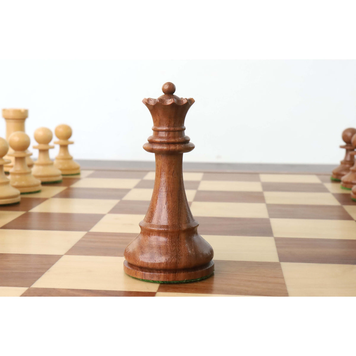 Golden rosewood French Grandmaster queen chess piece positioned on a wooden chessboard.