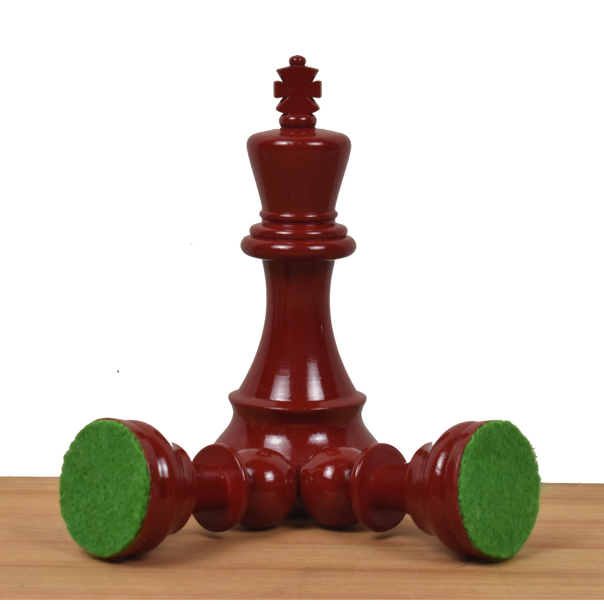 Standing burgundy Prime Staunton king alongside two fallen pieces displaying their green felt bases for board protection.