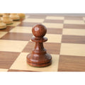 Golden rosewood French Grandmaster pawn chess piece standing on a wooden chessboard.