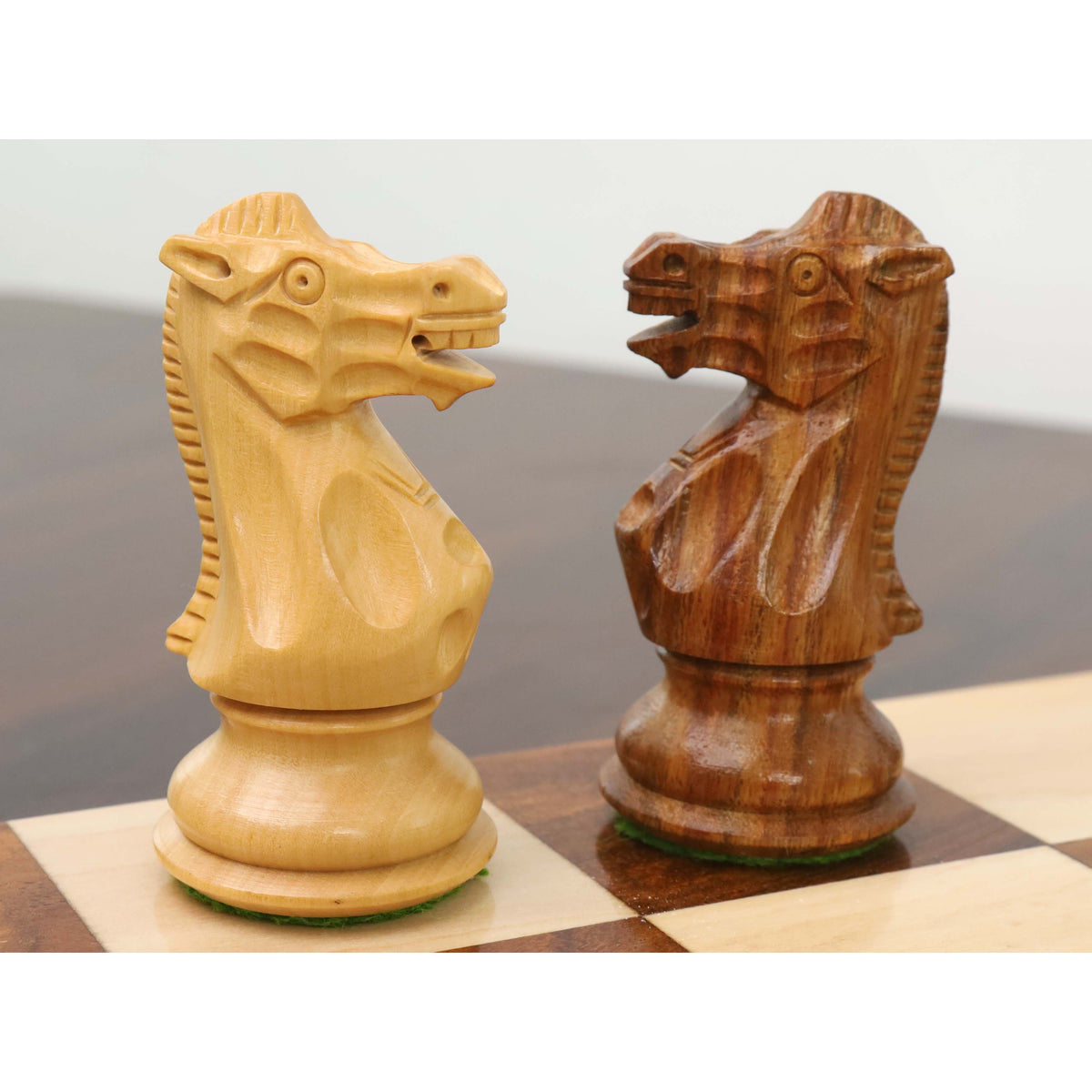 Boxwood and golden rosewood British Staunton knights facing each other on a glossy chessboard.