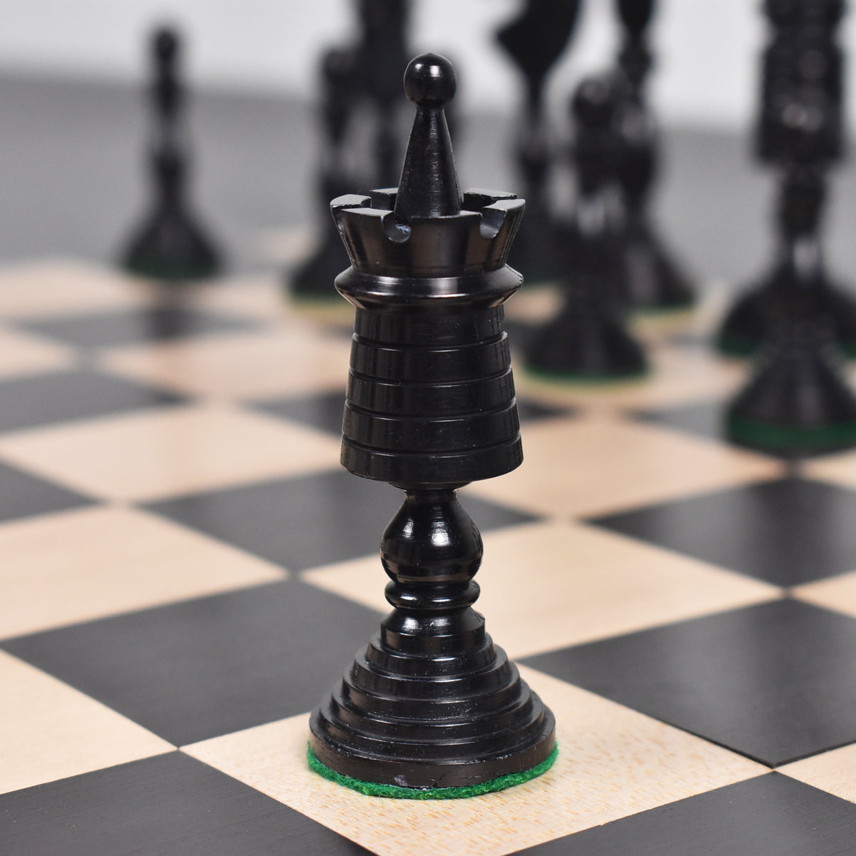 Black antique pre-Staunton rook chess piece positioned on a wooden board.