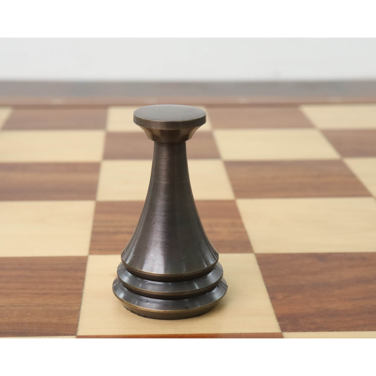 Single antique finish brass metal luxury chess pawn standing on a light square of a chessboard.