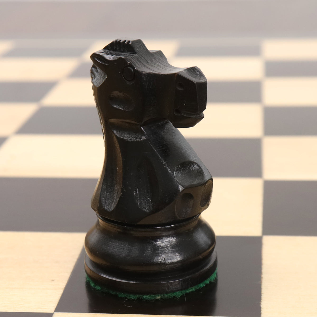 Close-up profile of a single ebonised boxwood knight from the Reykjavik Series Staunton chess set on a board.