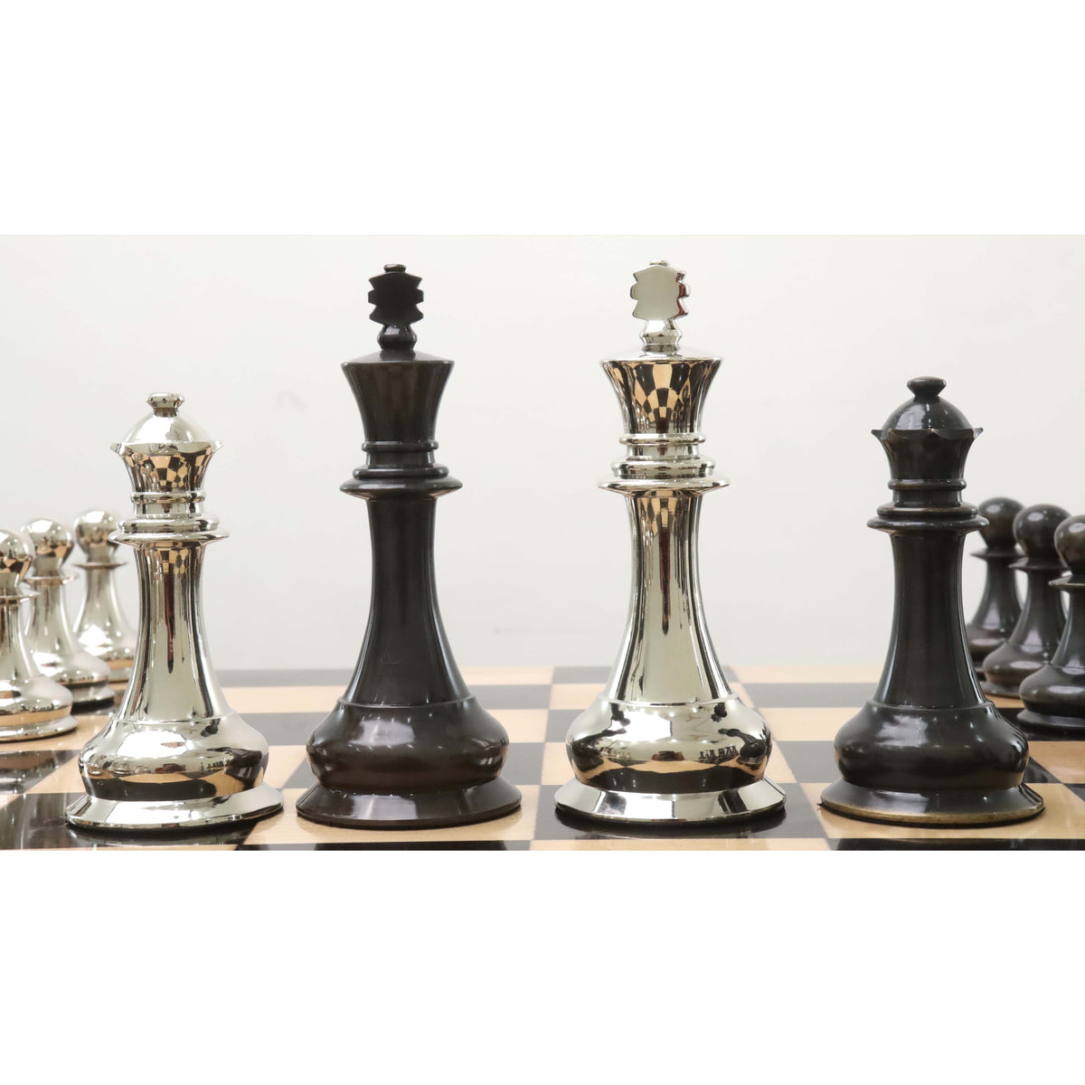 Polished silver and dark grey brass metal kings and queens lined up on a checkered board.