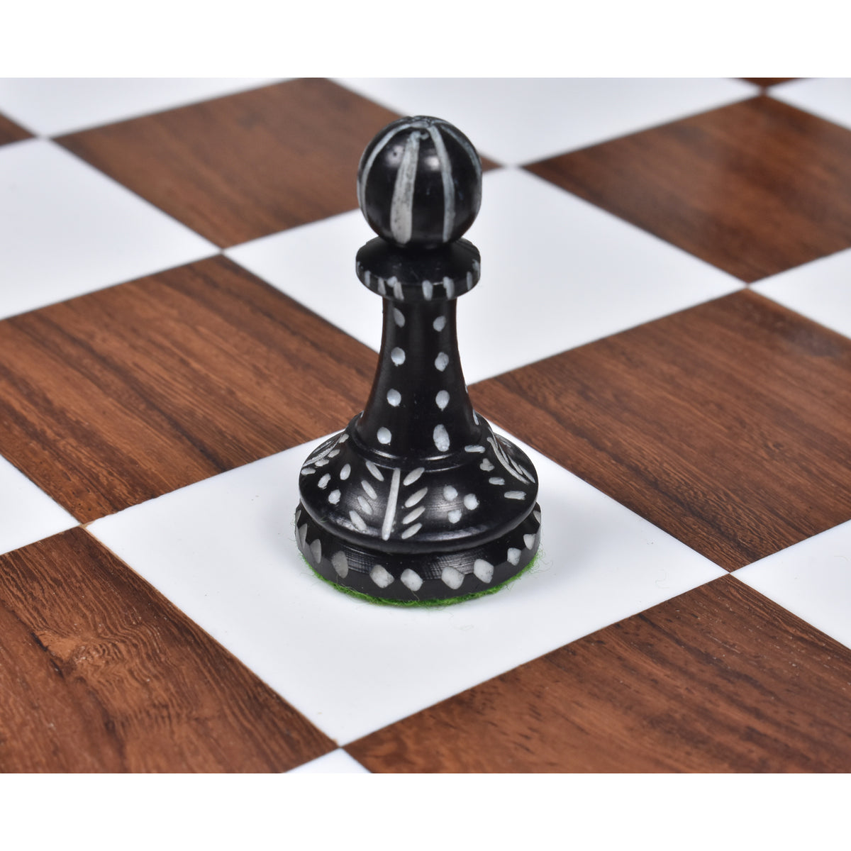 Single hand-carved black camel bone pawn chess piece on a wooden board.