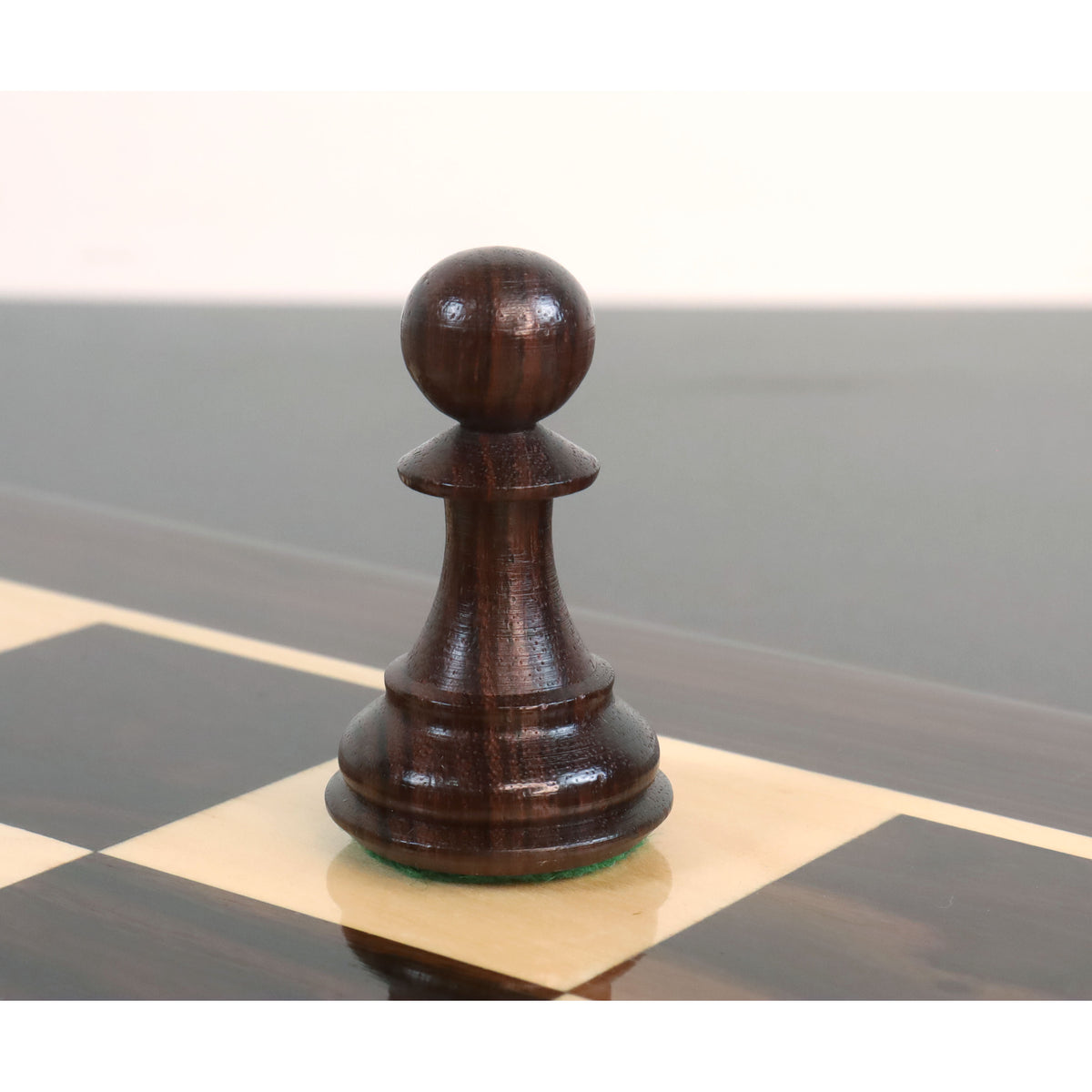 Close-up view of a dark rosewood pawn from the sleek Staunton luxury chess pieces resting on a glossy board.