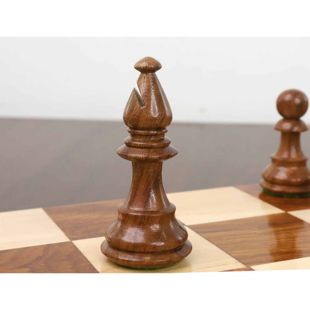 Close-up of a carved golden rosewood British Staunton bishop sitting on a wooden chessboard.