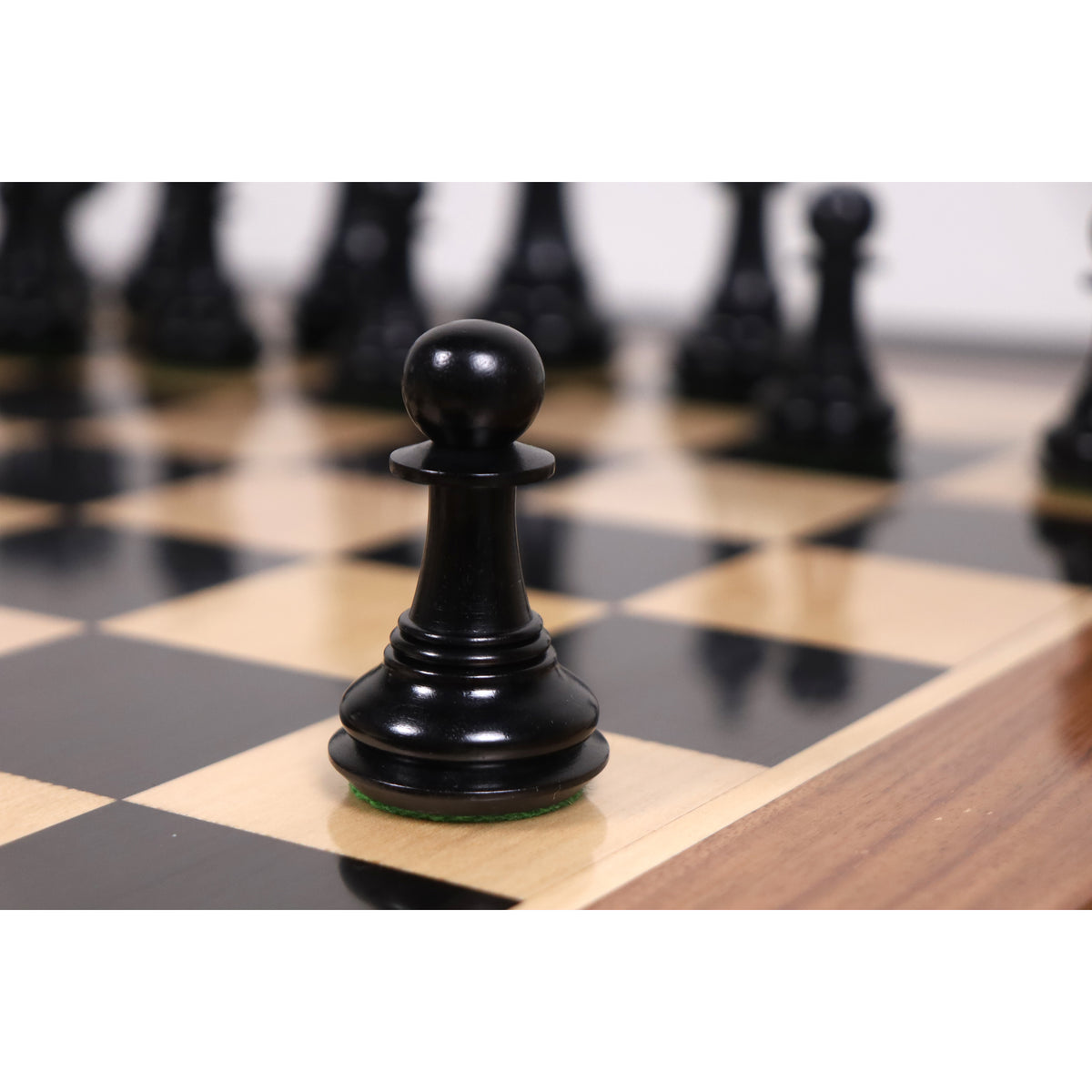 Black Spartacus luxury Staunton pawn standing on a wooden chessboard.