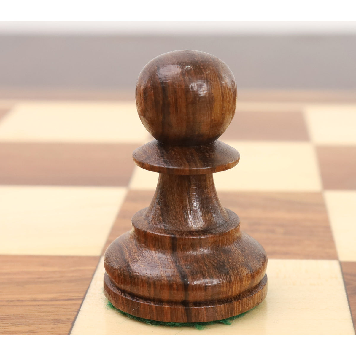 Close-up of a single golden rosewood pawn from the Reykjavik Series Staunton chess set on a board.