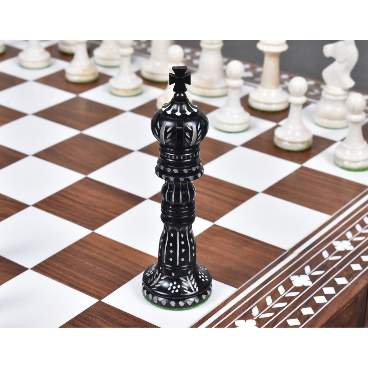 Hand-carved black camel bone king chess piece on an inlaid wooden board.