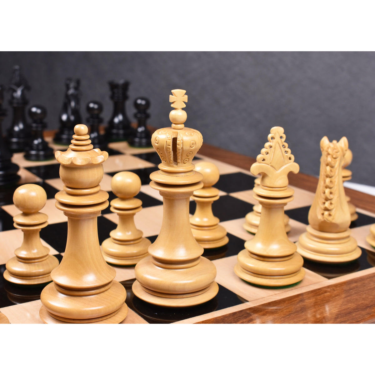 Low-angle perspective of the ornate boxwood king and queen pieces on a premium chessboard.
