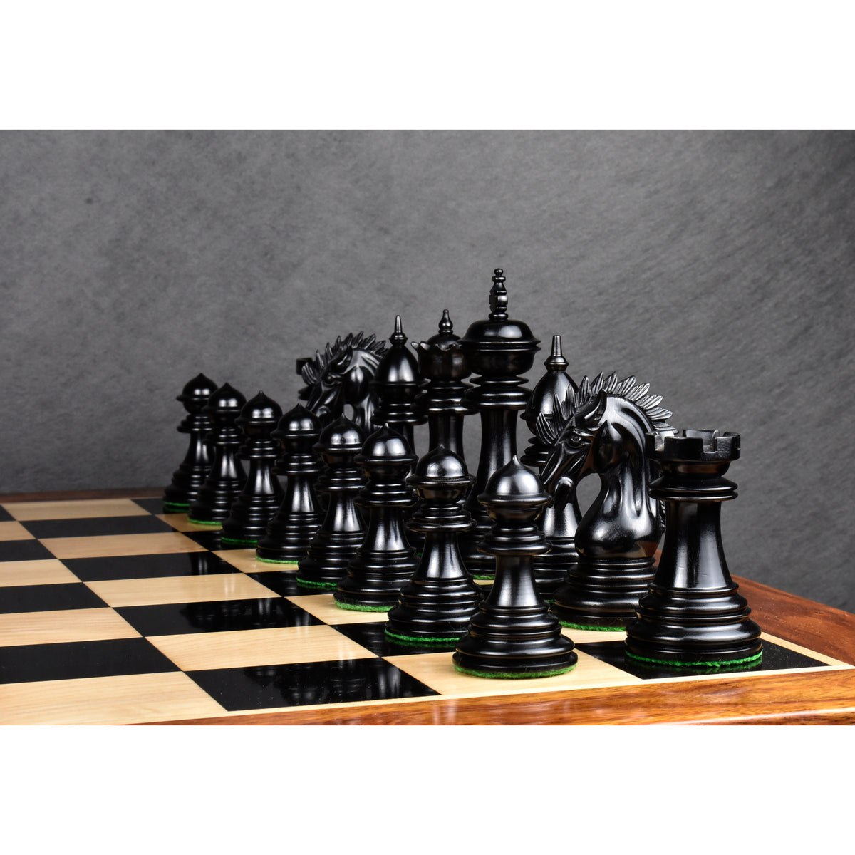 Polished dark ebony wood chess pieces set up in starting formation on a glossy wooden chessboard.