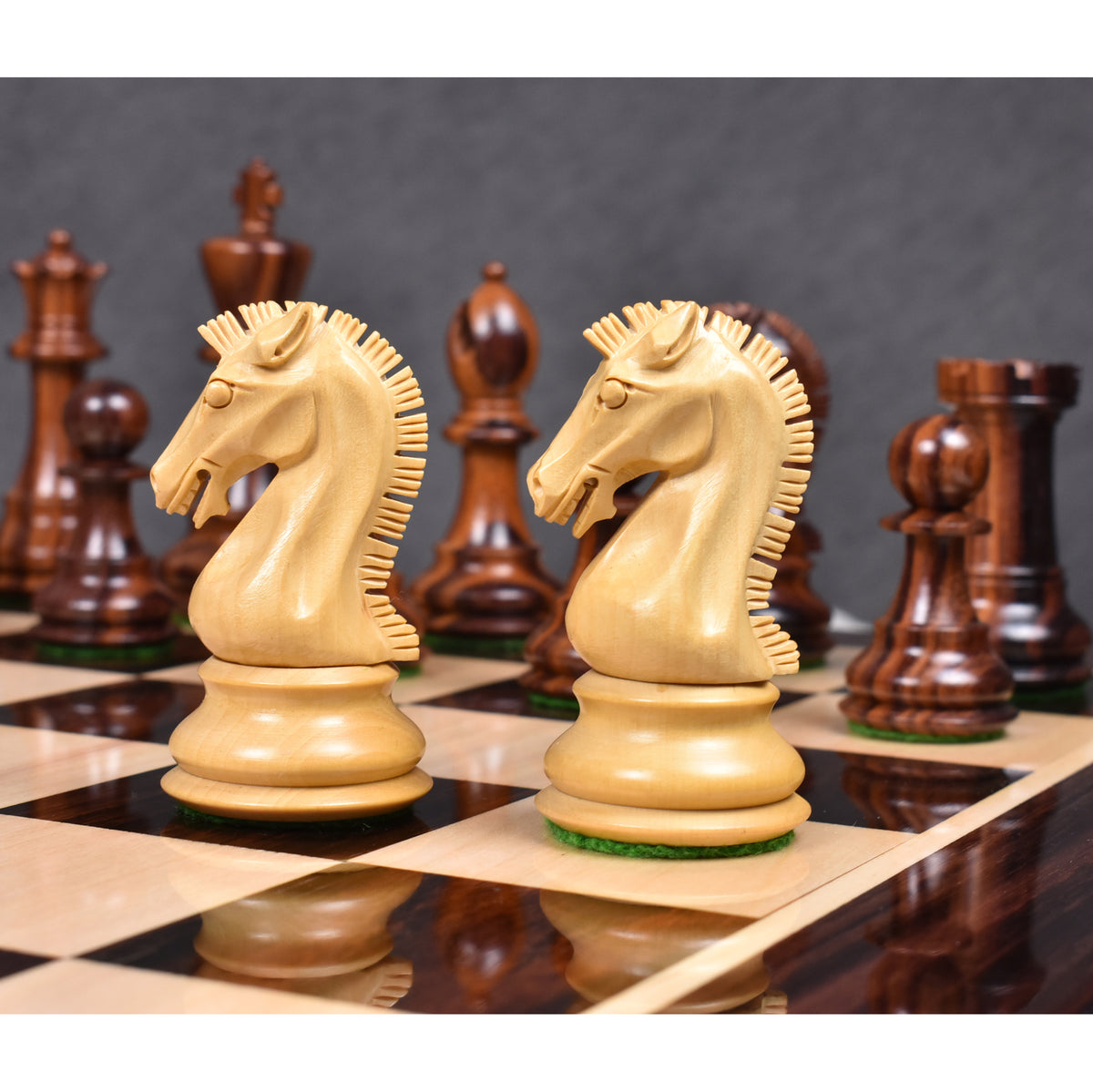 Two light boxwood knights from the 3.9" Craftsman Staunton chess set standing on a board with a blurred background.